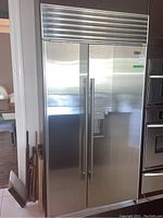 Full front view of the installed stainless steel refrigerator with two doors and top vent grille