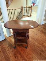 Wooden drop leaf tea cart with scalloped edges, shown fully open from front angle on wood floor.