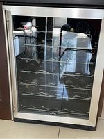 Front view showing stainless steel frame, glass door, internal wave shelves and wine bottles