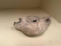 Side view of the ancient pottery oil lamp showing the round body, filler hole and damaged spout.