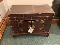 Front view of wooden campaign chest with metal corner reinforcements, double front doors, and a base with bracket feet.