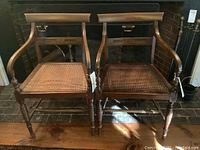 Pair of wooden arm chairs with caned seats placed side by side, showing general view and condition.