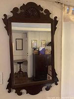 Full view of the rectangular Chippendale style mirror hanging on the wall showing the carved edges and the wood frame.