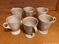 Front and angled view of six footed coffee cups arranged in two rows showing handles and the cup shape, highlighting the color, footed base, and overall condition including crazing and discoloration.
