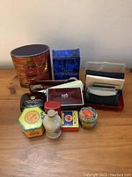 Photo showing all items in the lot on a wooden surface including boxes, tins, compact mirror cases and the liniment bottle.