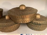 Close-up of three brass bowls stacked showing geometric etched pattern and rounded lid knob