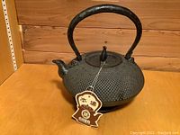 Front angle view of textured cast iron tea kettle with handle, spout, lid, and attached tag with Asian characters.