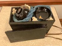 Wooden box open showing black lacquer bowls with gold designs, blue cloth bag inside for protection.