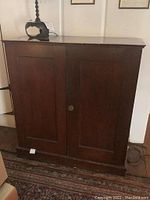 Front view of large wooden cabinet showing two paneled doors and metal knobs.