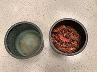 Top view of the two metal bowls. One bowl is empty showing interior wear and damage at bottom rim. The other bowl contains dried potpourri in shades of brown and red.
