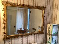 Full frontal photo of the large rectangular mirror with a painted gold carved frame hanging on a wall, showing the overall size and style in a home environment.