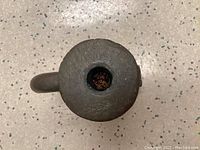 Top-down view of an antique metal mortar showing its round flat surface and handle.