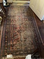 Full view of the worn rectangular Oriental rug placed on wooden floor showing overall faded geometric and floral patterns in earthy tones