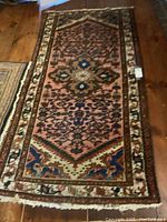 Full view of the small runner rug laid flat on wood floor showing overall condition and colors.