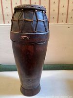 Full view of the primitive drum showing its tall wooden body and drumhead tensioned by wooden slats.