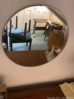 Frameless round mirror mounted on wall, showing reflection of furniture and room interior.