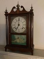 Front view of complete wooden Seth Thomas mantel clock showing upper clock face with Roman numerals and lower painted glass panel depicting a house.
