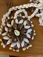 Close-up of floral shell pendant with white, brown, and some red shells arranged in a flower shape, on a wooden surface
