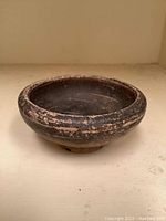Side view of a small, dark glazed ceramic bowl on a flat surface, showing its round shape and raised base.