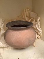 Front view of a small old clay pot showing its rounded body resting on tissue paper.