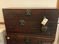 Front view of dark wood chest showing two large drawers with iron handles and circular iron hardware accents.
