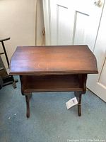 Front angled view showing the slanted top and open book storage underneath of the vintage wooden table.