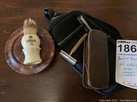 Complete view of shaving set with brush on bowl, black mug, two safety razors, zipper zippered case and leather blade case.
