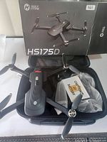 Holy Stone HS175D drone displayed with carrying case and battery in original box, showing top side of the drone and propellers.