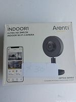 Front of the Arenti Indoor Wi-Fi camera box showing the camera image and a mobile phone with the app interface.