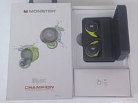 Opened box showing Monster iSport earbuds in black and lime green with charging case inside.