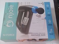 Front packaging of NJOIE N•FORCE Professional Percussion Massage Gun showing the product image and main features such as deep massage therapy, five-speed settings, improved circulation, and workout recovery benefits.