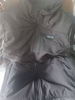 Front view of black Ptahdus heated jacket with chest pocket and visible heating control buttons.