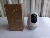 Security camera and original packaging box on a white table.