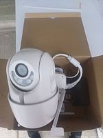 Photo of the white dome-shaped Wi-Fi Cloud Camera inside an open cardboard box showing lens and cables.