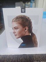 Front view of the Mini wireless earbuds packaging showing a profile of a woman wearing the earbud and brand logo.