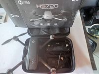 Holy Stone HS720 foldable drone placed inside a black carrying case, with remote controller, charging cables, and original box in the background.