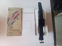 Black I-Miata smart watch with black silicone band, original packaging box, and user manual displayed on white surface.
