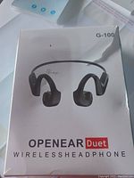 Front of box showing OPNEAR Duet wireless headphones G-100 in sealed retail packaging with minor wear and tear.
