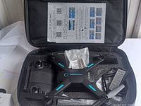 Open black zippered carrying case with foam insert showing Zuhafa brand drone, remote controller, props, and a manual inside case lid.