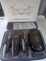 Top view of the foldable drone and remote controller inside a black foam compartment with box packaging showing a line drawing of the drone.