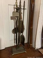 Full view of brass fireplace tool set on stand with seven pieces including broom.