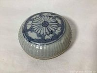 Closed view of the ceramic ink pot showing top lid with blue floral pattern and textured sides