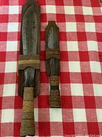 Front view of both daggers sheathed showing rustic wooden sheath and cord-wrapped handles with metal blades inside.