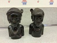 Front view of the pair of dark stained hand carved wood busts showing facial details and necklaces