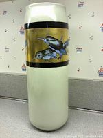Full view of the tall cylindrical hand-painted vase showing white porcelain with a wide gold band bordered in black containing bird paintings.