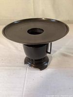 Complete view of assembled bronze Ikebana vase, showing tripod base with handle and wide circular top plate with central hole.