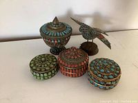 View of the three Pala amulet boxes in turquoise, green, and red glass beads with brass, plus the bird figurine on a wooden base.
