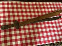 Full view of the Philippine sword next to its sheath on a red and white checkered cloth.