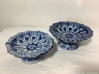 Photo of two blue and white footed ceramic compote bowls side by side showing scalloped edges and floral geometric decoration