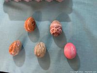 Five polished stone eggs in various natural colors and patterns arranged on a blue-green cloth.